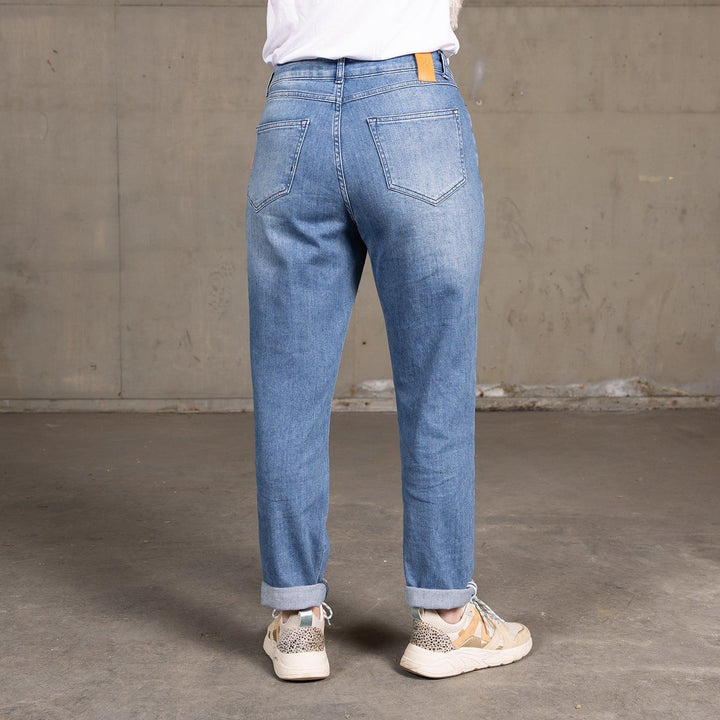 Achteraanzicht van een model dat The Mom jeans van Delft Denim draagt. Deze duurzame mom jeans heeft een relaxte pasvorm, een lichte denim wassing en een omgeslagen zoom voor een casual en comfortabele uitstraling.
