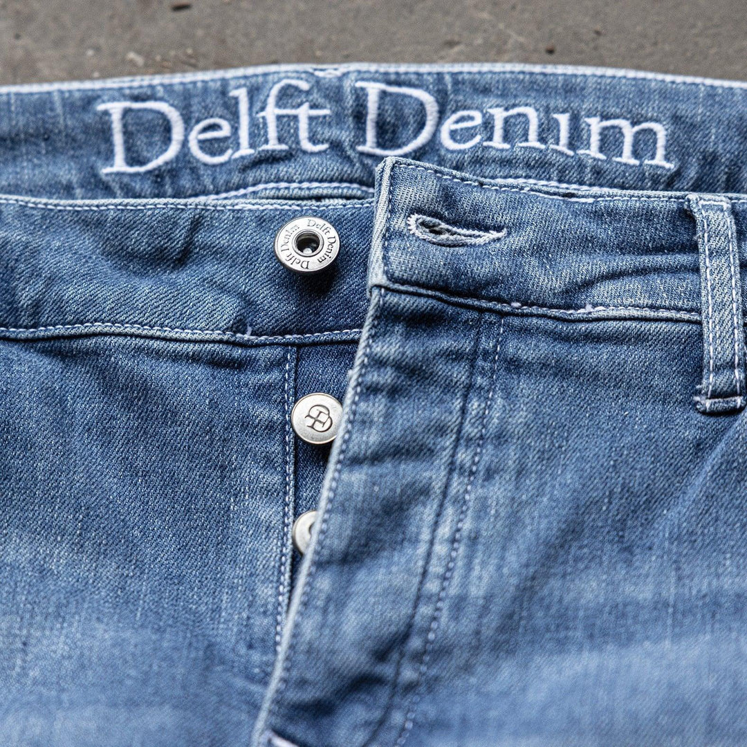 Detail van The Slim jeans van Delft Denim – duurzame slim-fit spijkerbroek met knoopsluiting en geborduurd logo. Gemaakt van biologisch en gerecycled katoen voor comfort.